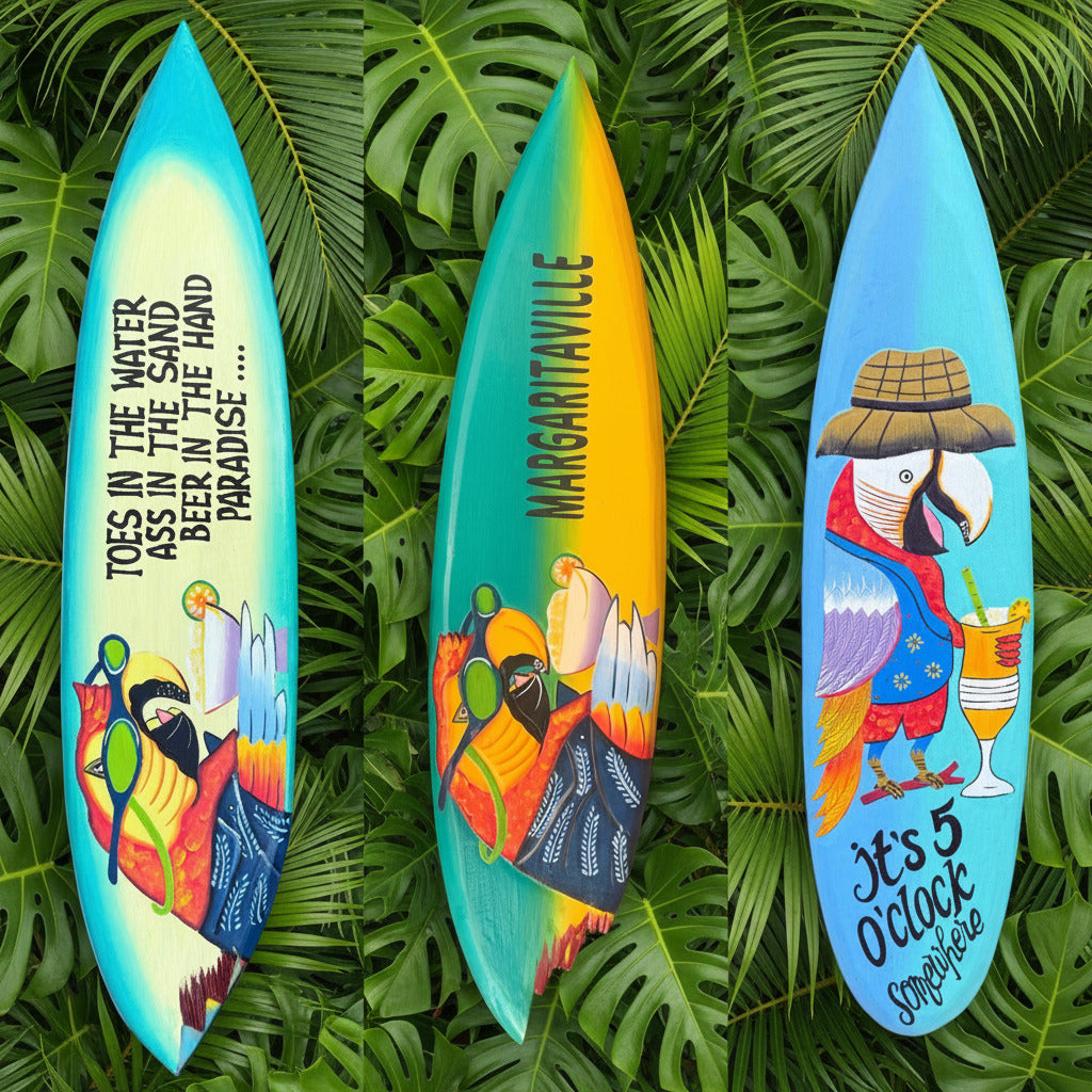 Three colorful hand-painted surfboard-shaped signs displayed outdoors on sand next to wooden posts. Each sign features a different tropical design: a blue sign with a parrot and the text 'TOES IN THE WATER HASS IN THE HAND PARADISE .