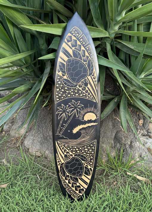 Decorative surfboard with tribal turtles and a surfer catching a wave.