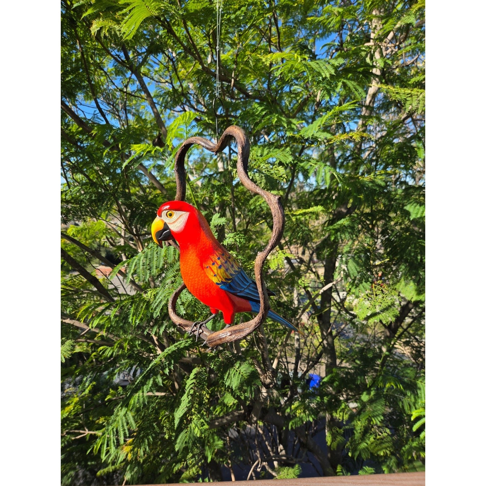 Decorative parrot ornament on a branch against a green tree background