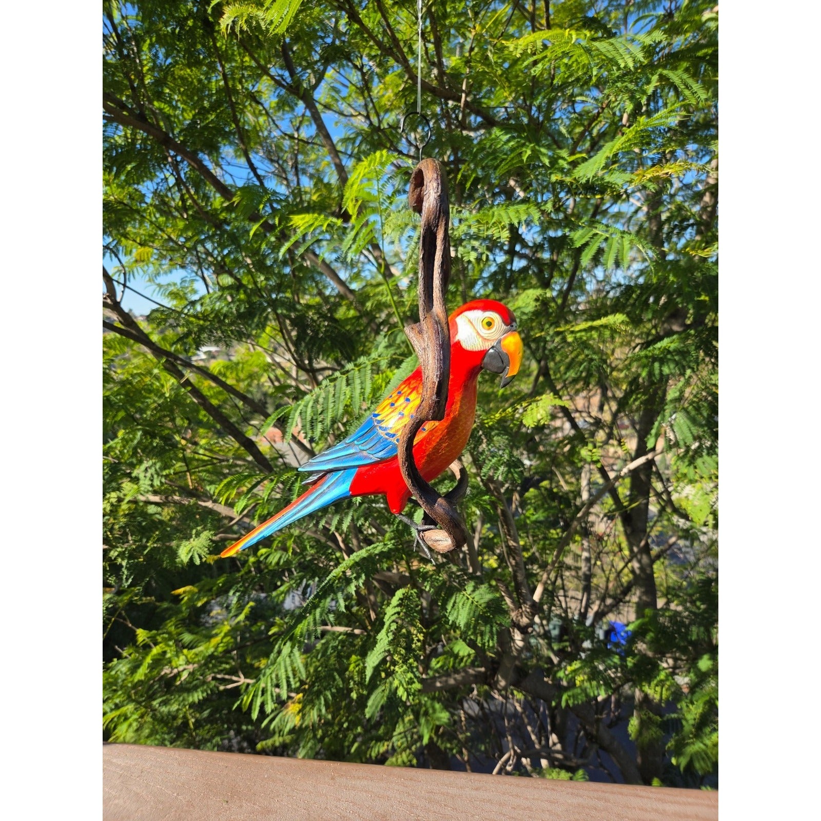 Colorful parrot figurine hanging from a branch with a natural green background