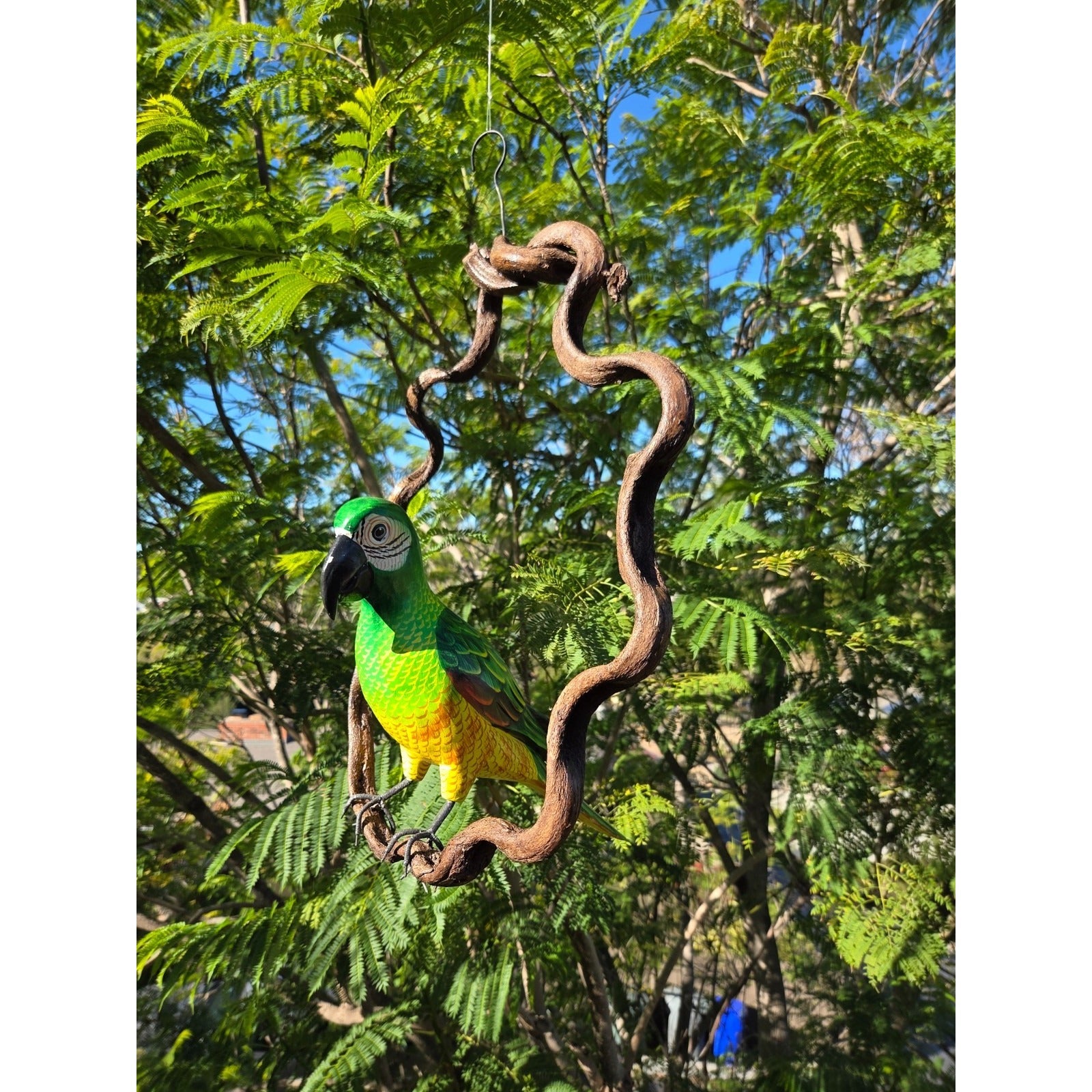 Decorative parrot ornament hanging from a branch with green foliage in the background