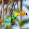Decorative toucan ornament hanging from a branch with a blurred natural background
