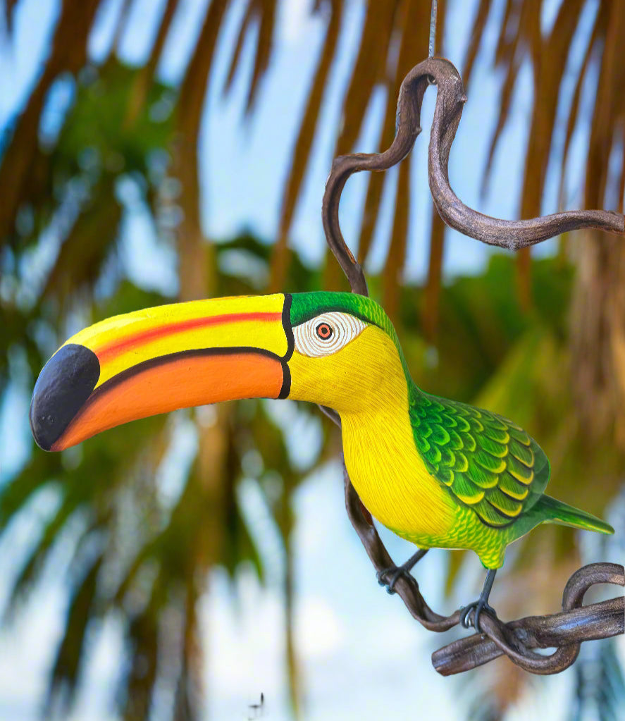 Colorful toucan bird figurine perched on a branch with blurred green foliage in the background