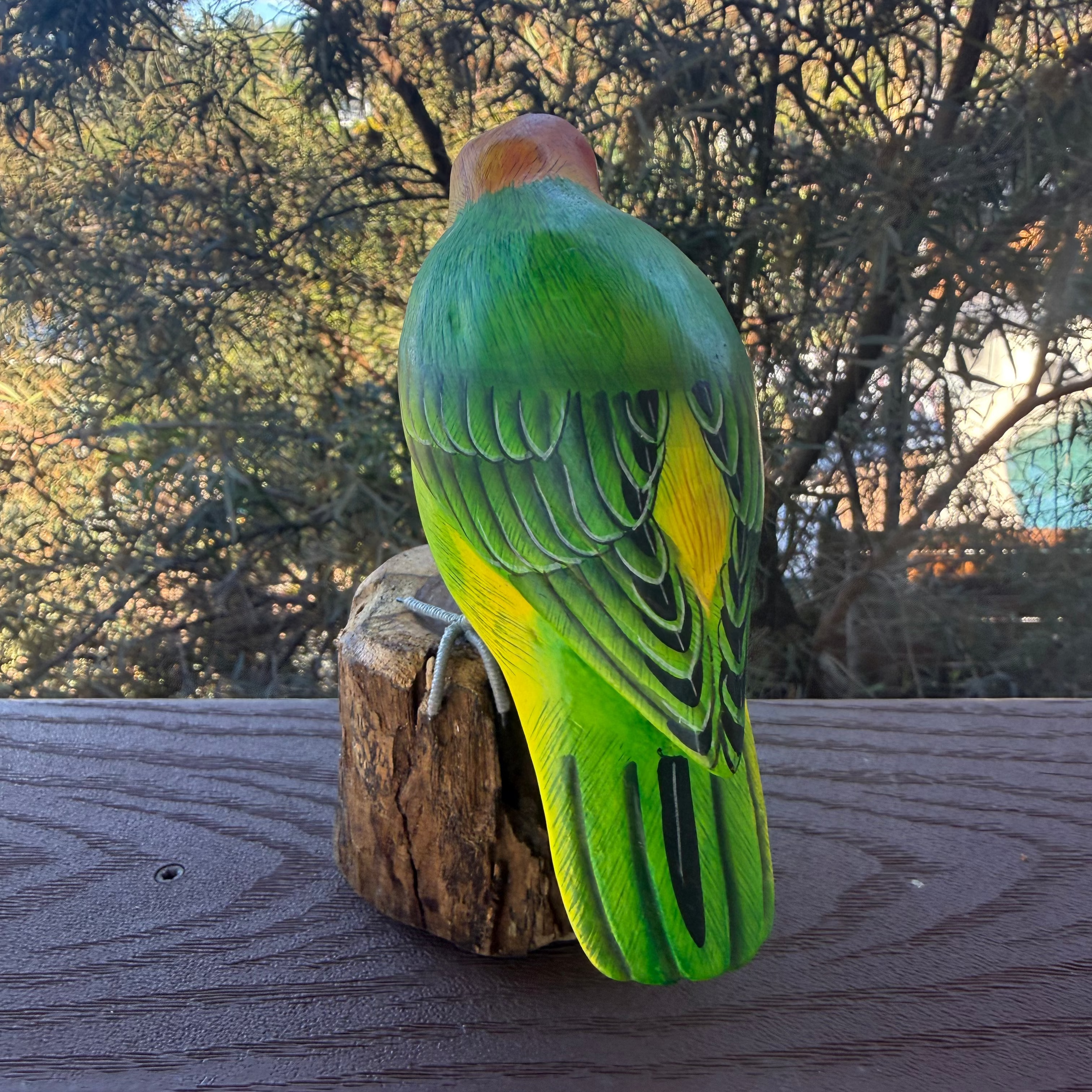 Colorful parrot figurine on a wooden surface with trees in the background