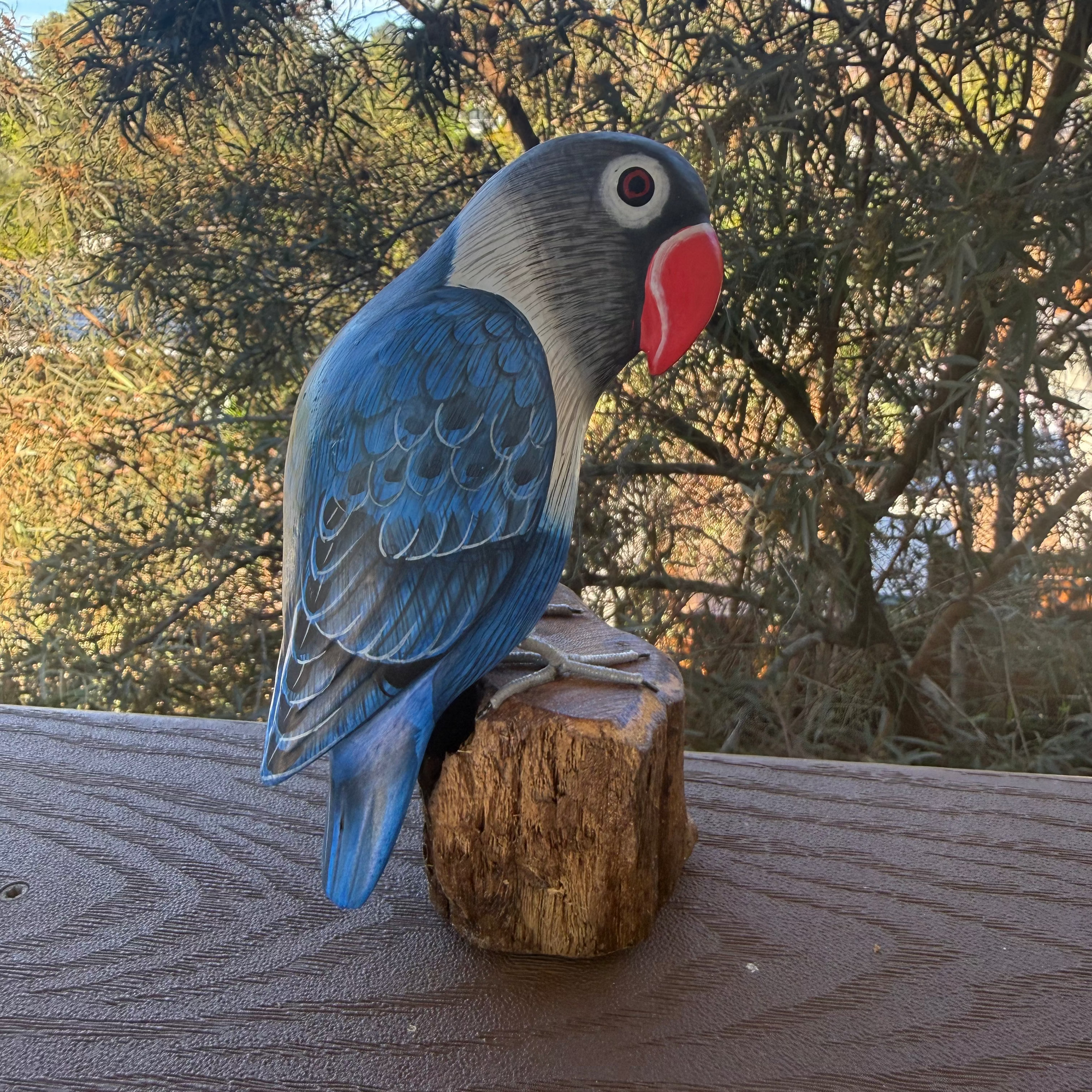 Wooden parrot figurine on a wooden surface with trees in the background