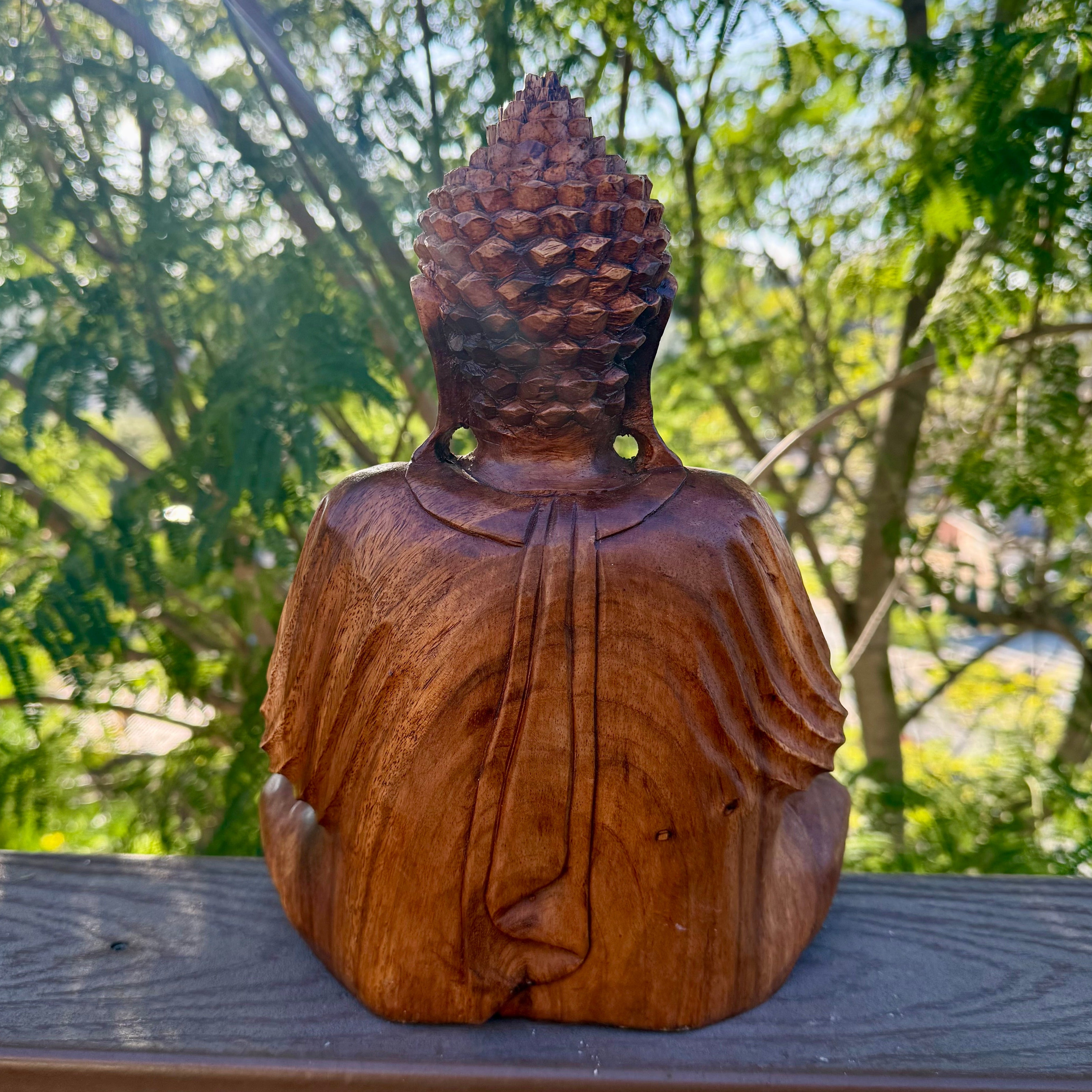 Wooden Buddha statue outdoors with greenery in the background