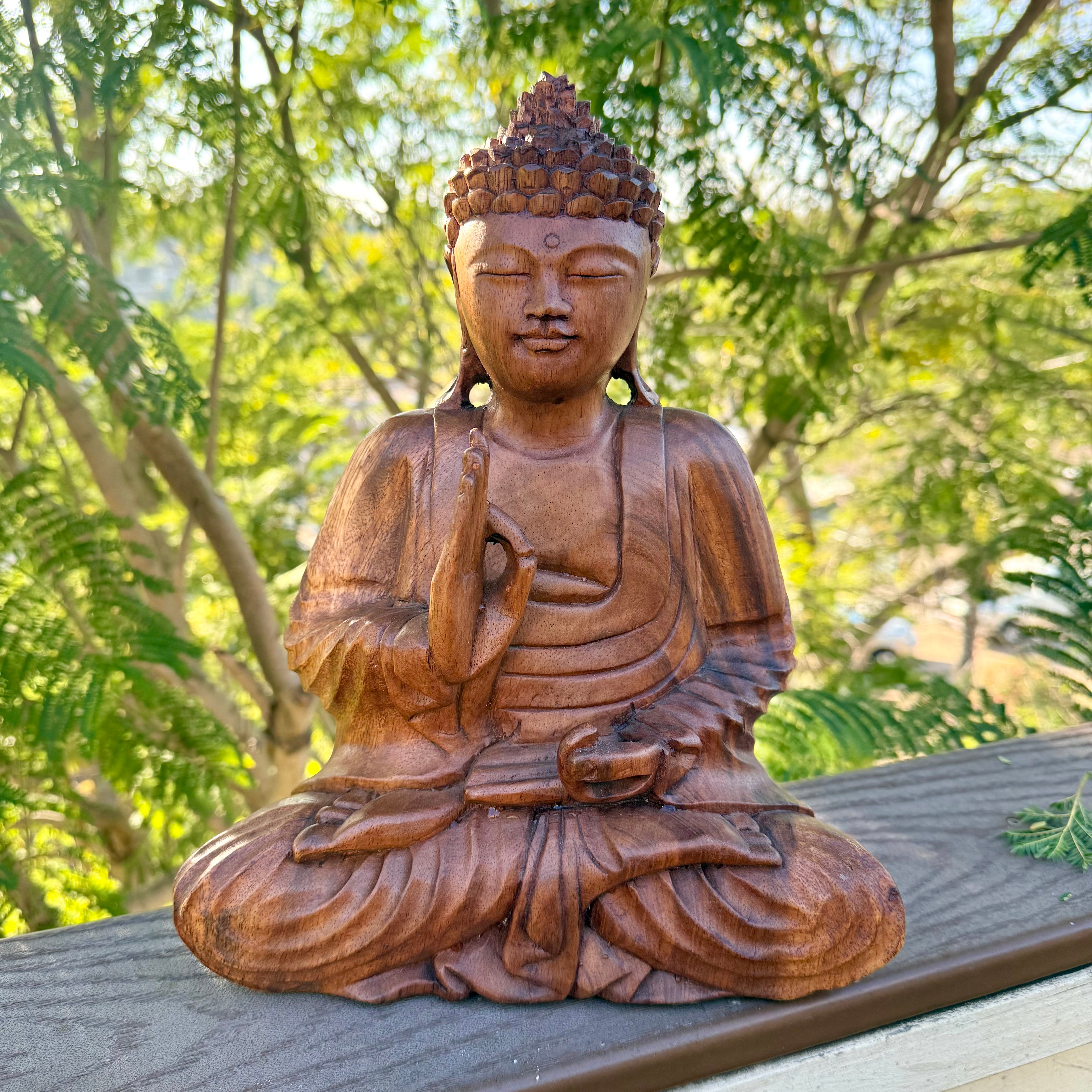 Wooden Buddha statue outdoors with greenery in the background