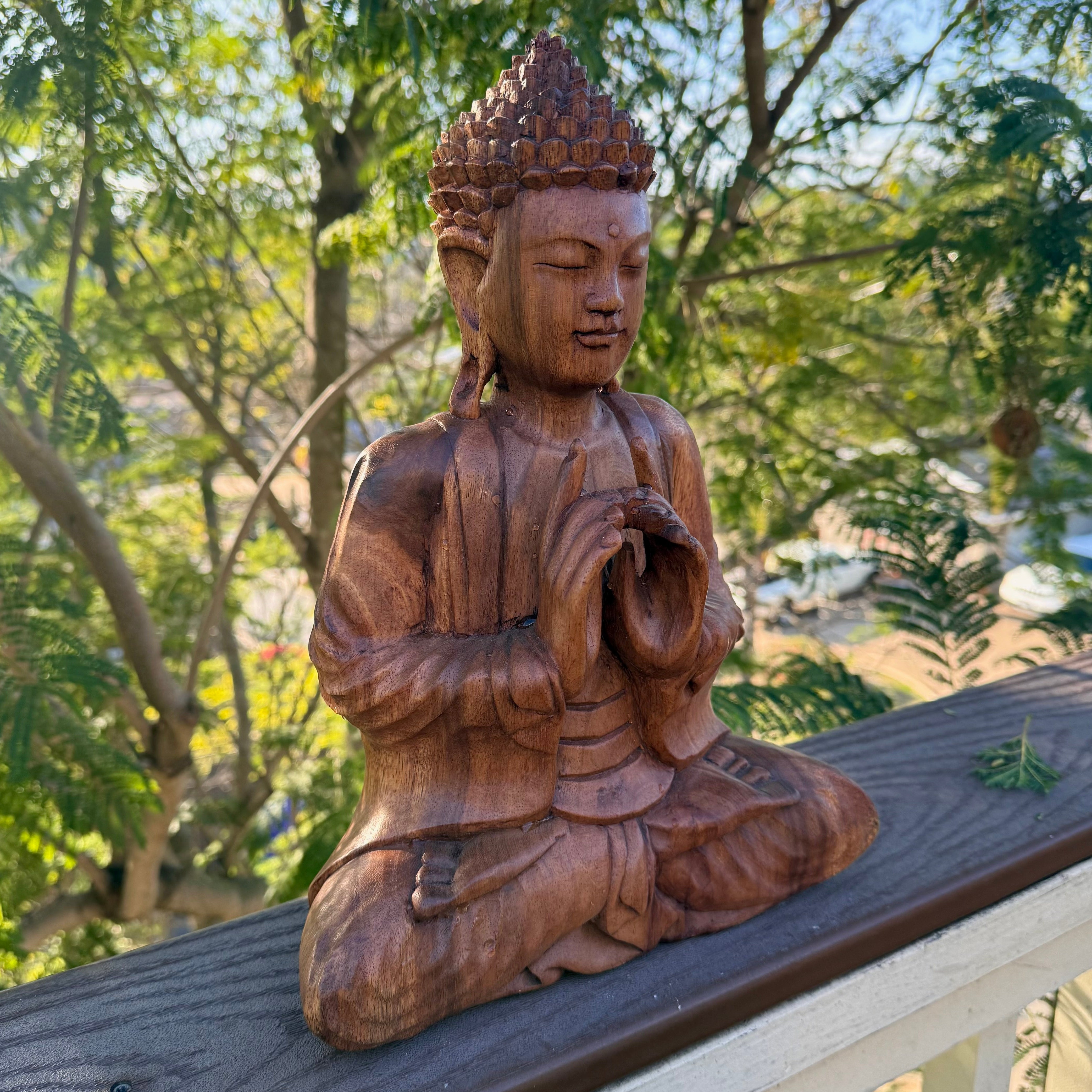 Wooden Buddha statue outdoors with greenery in the background