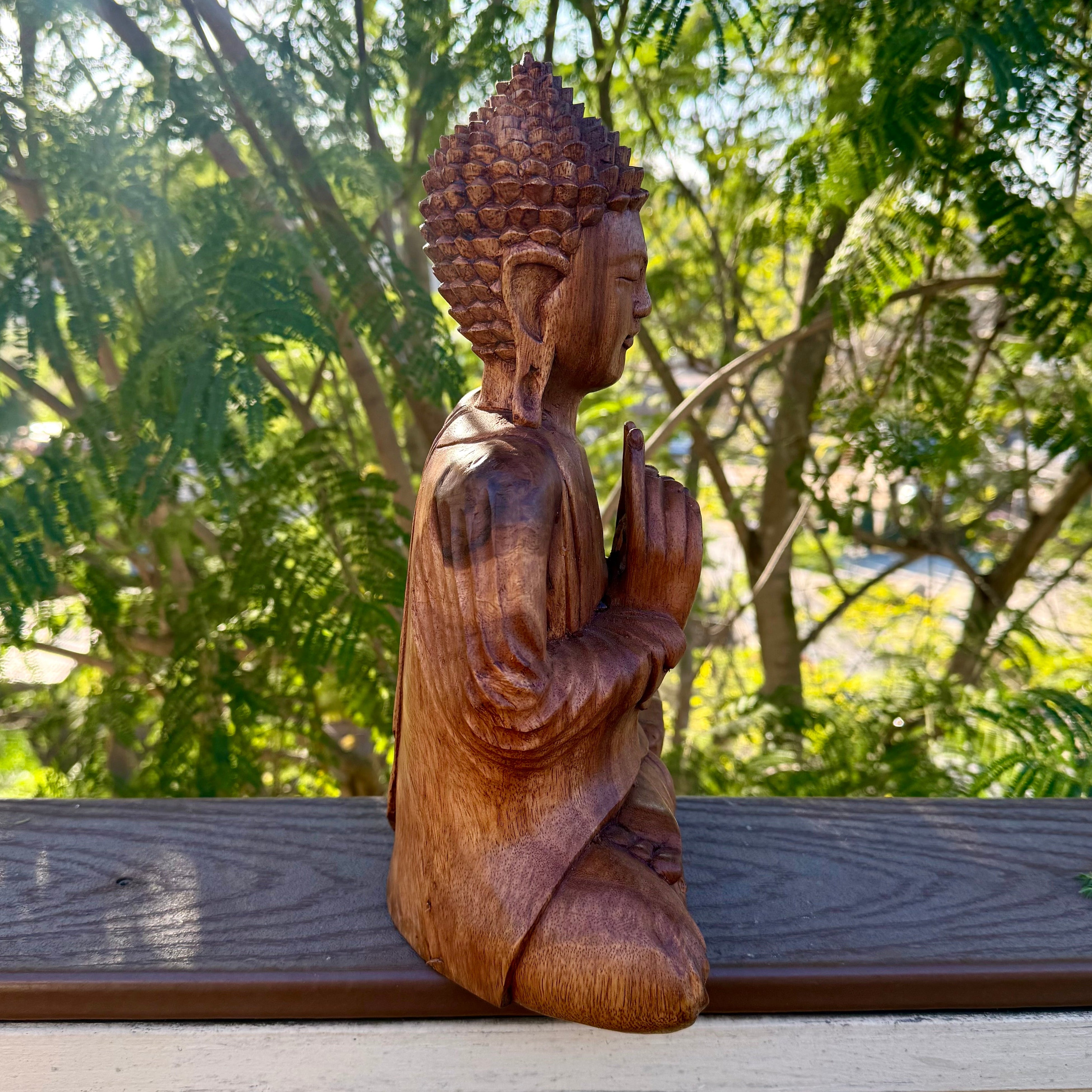 Wooden Buddha statue on a wooden platform with greenery in the background