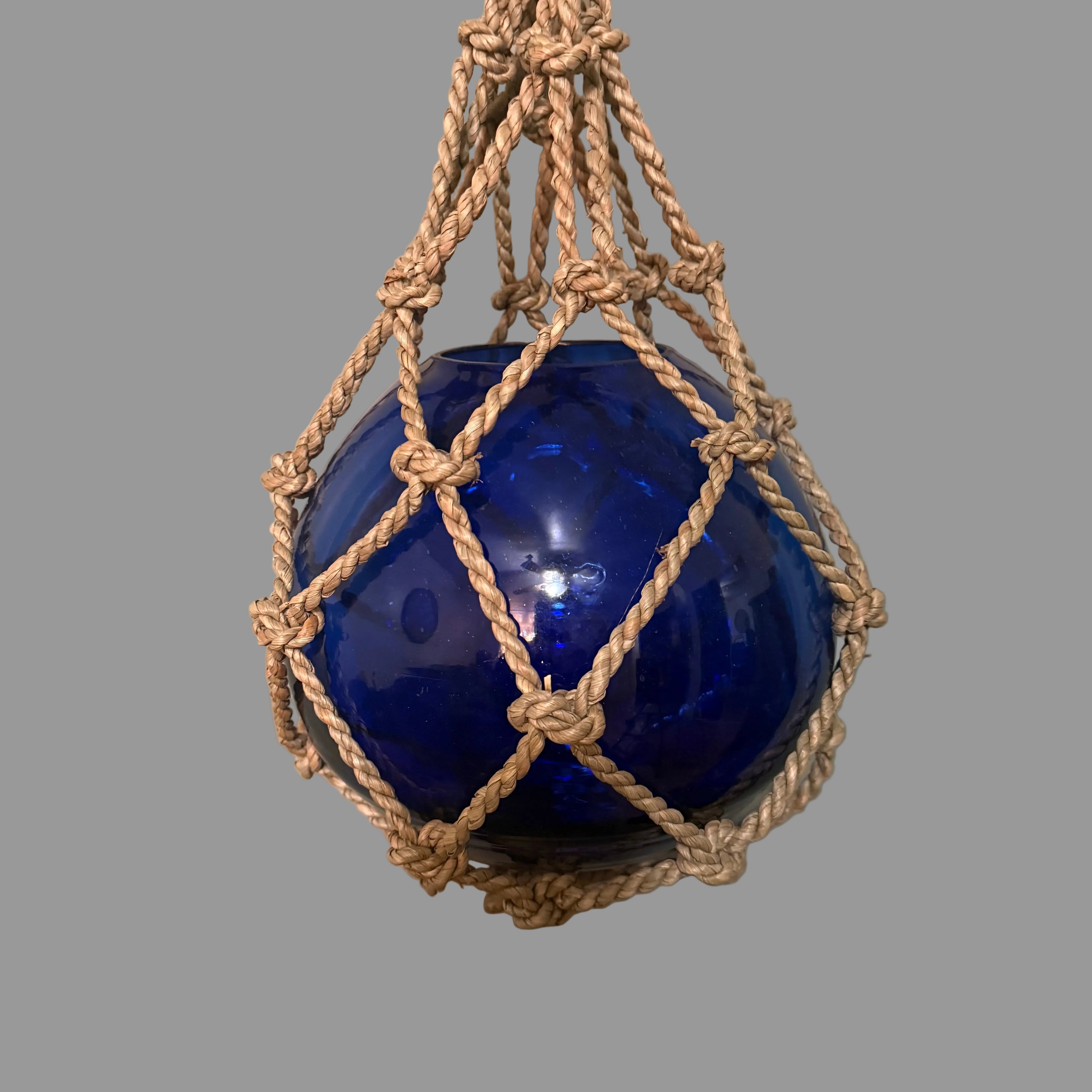 Blue buoy suspended by a rope against a plain background