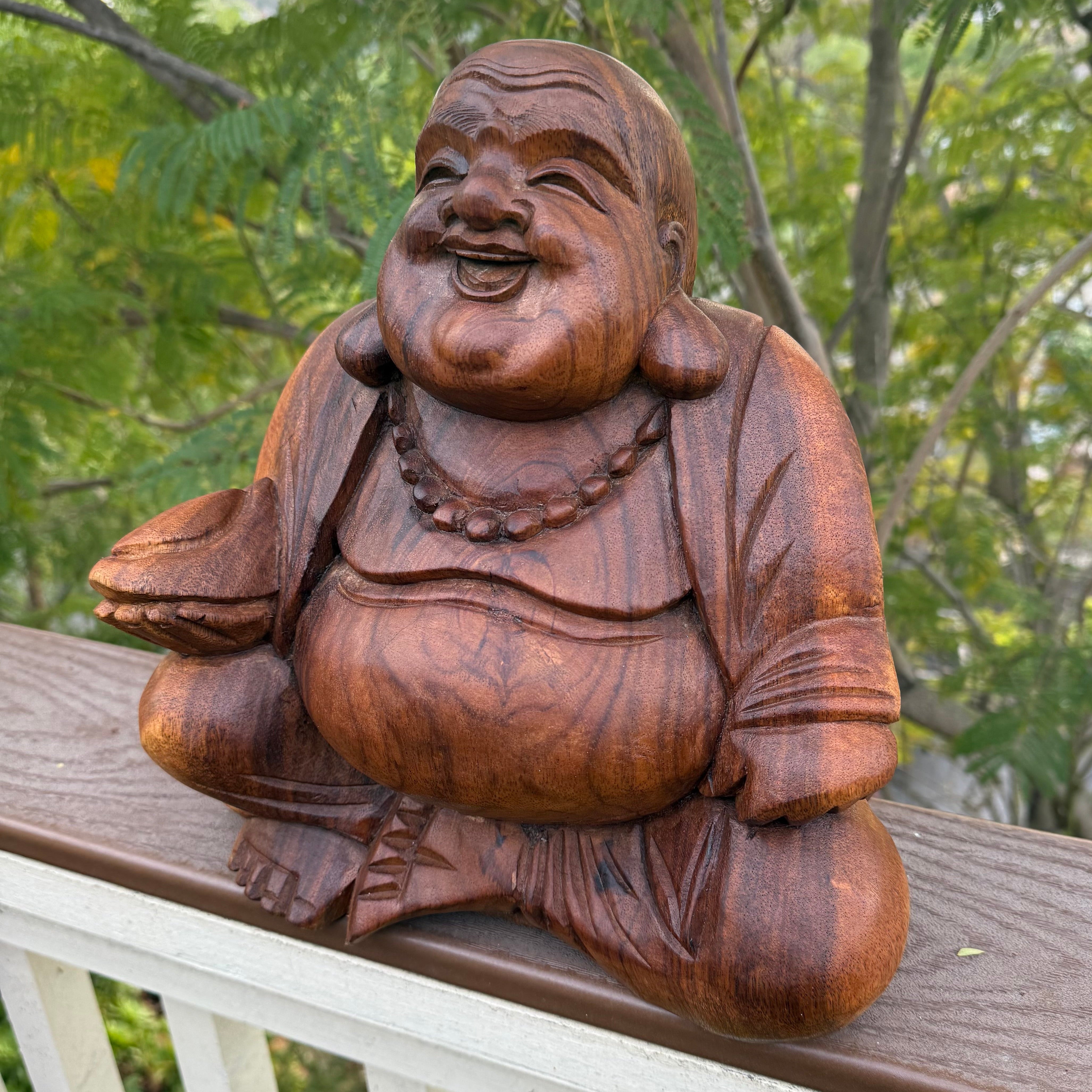 Wooden Buddha statue on a railing with greenery in the background