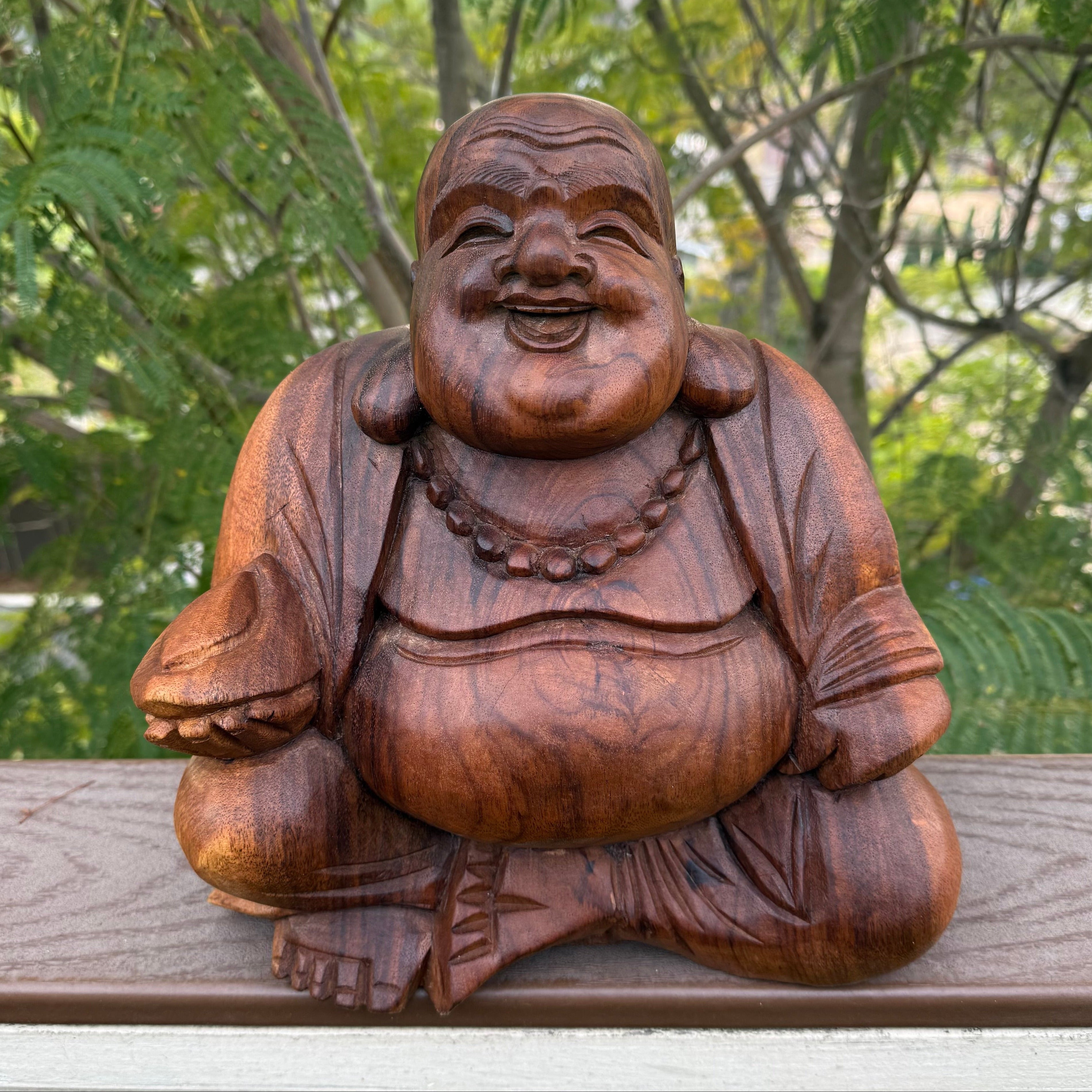 Wooden Buddha statue on a wooden surface with greenery in the background