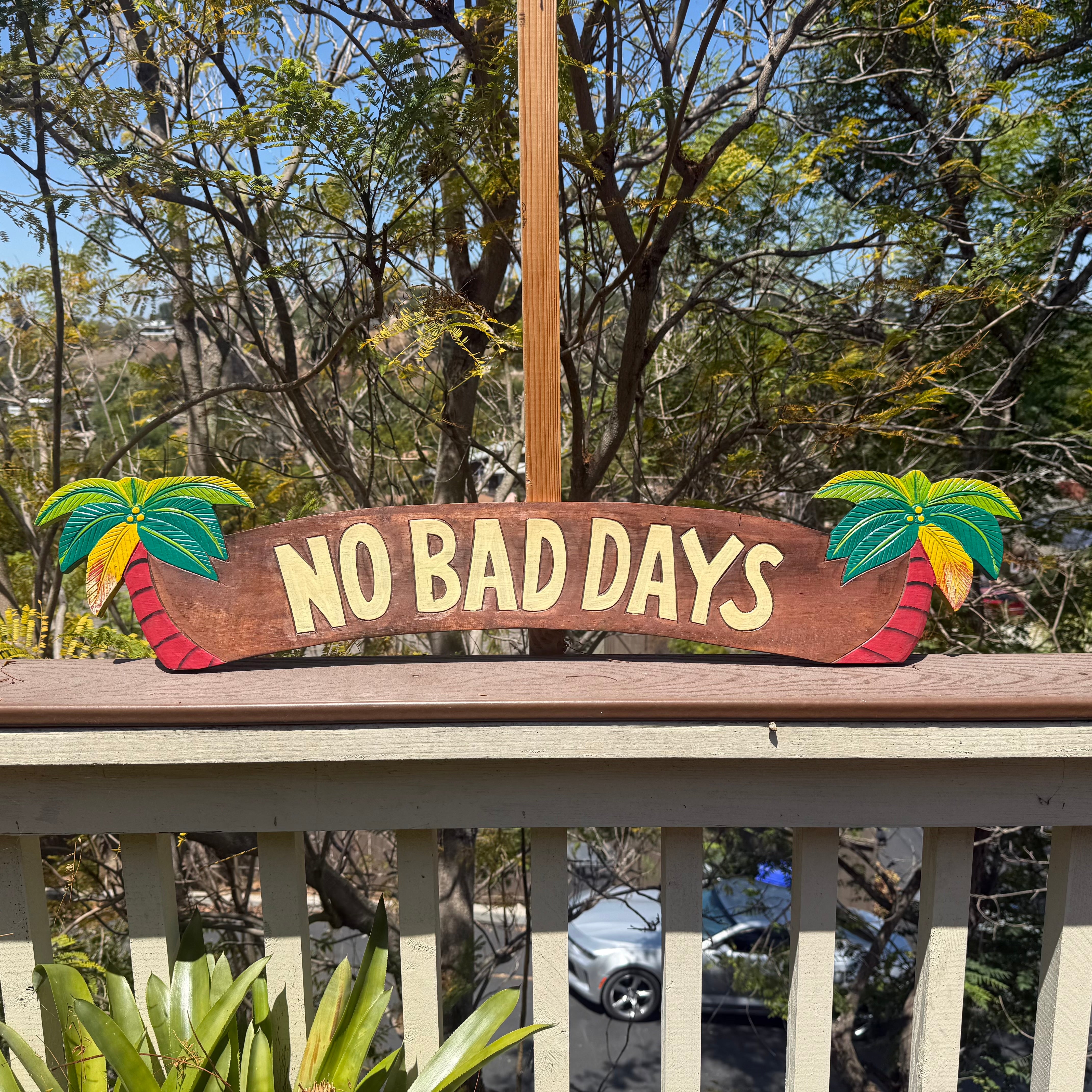 Wooden sign with 'NO BAD DAYS' on a railing with trees in the background