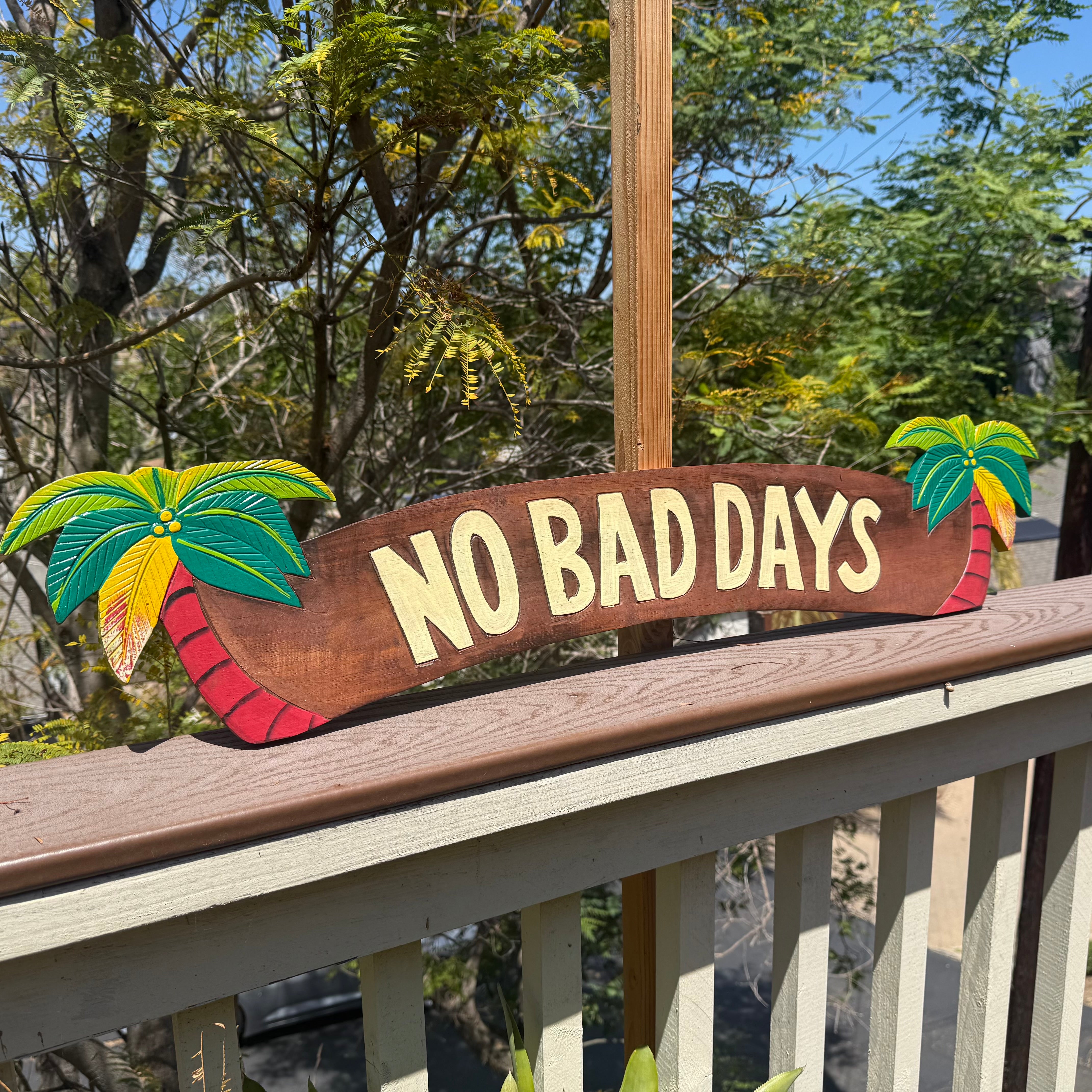 Decorative sign with 'NO BAD DAYS' on a railing with palm tree designs, outdoors.