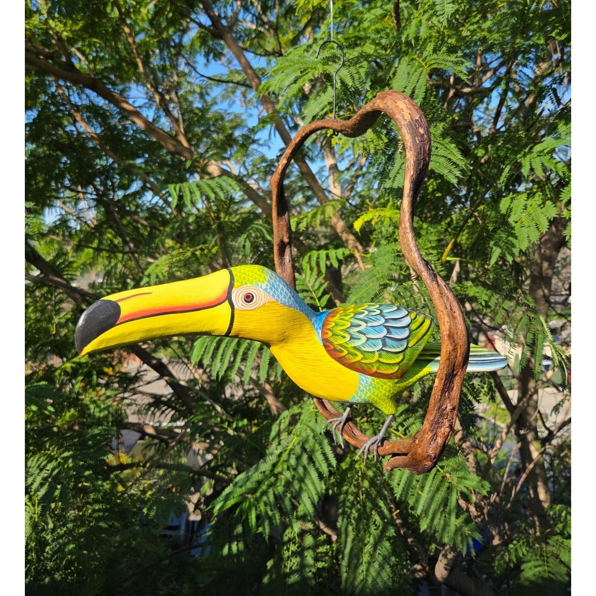 Colorful toucan figurine perched on a branch with a natural background of green foliage.