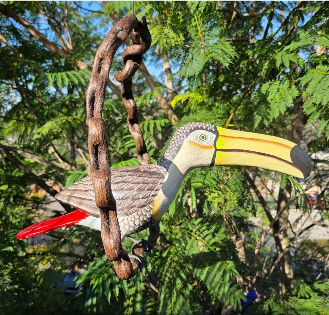Decorative toucan Statue on a branch with a natural background of green foliage.