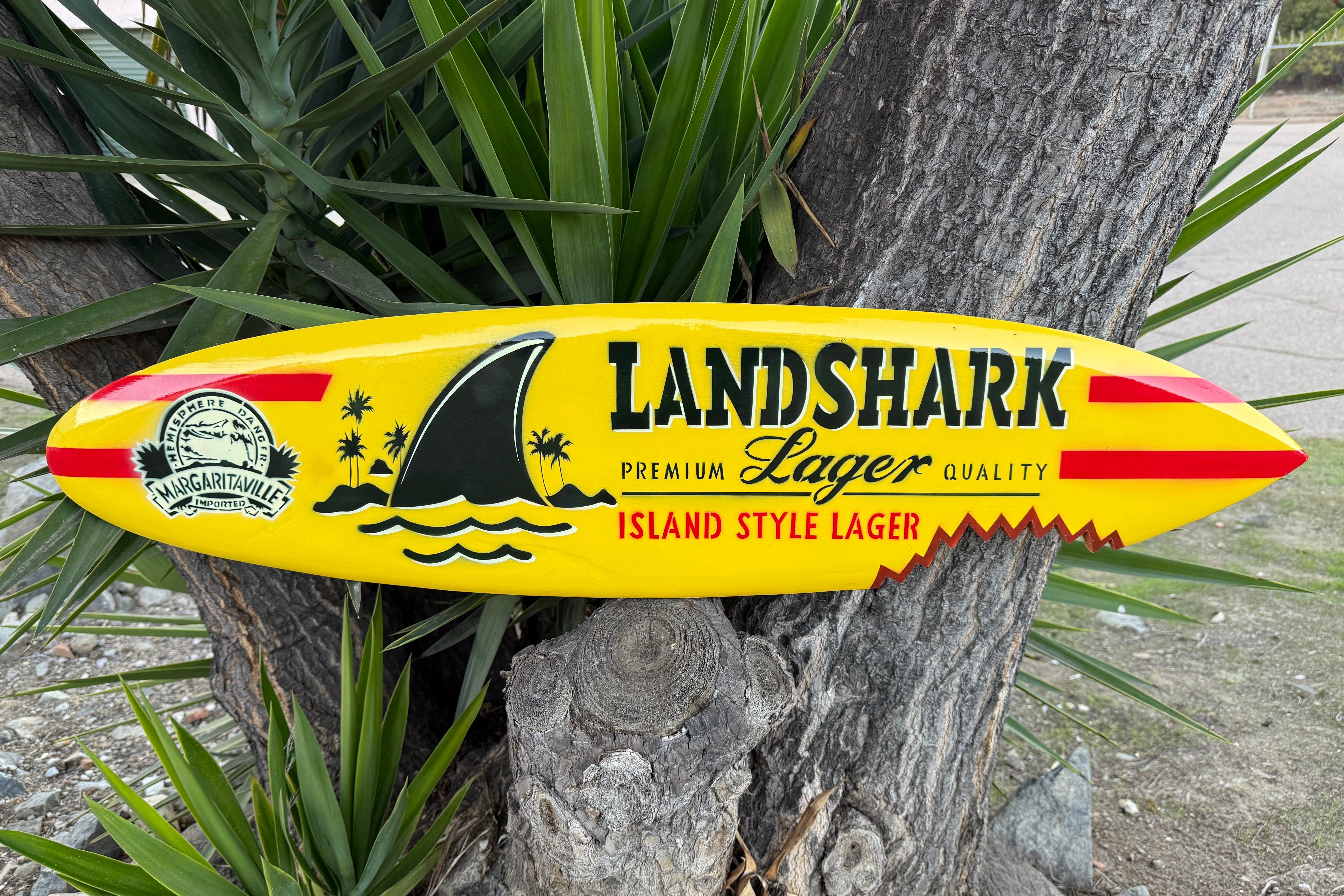 Yellow Landshark Lager surfboard-shaped sign against a tree