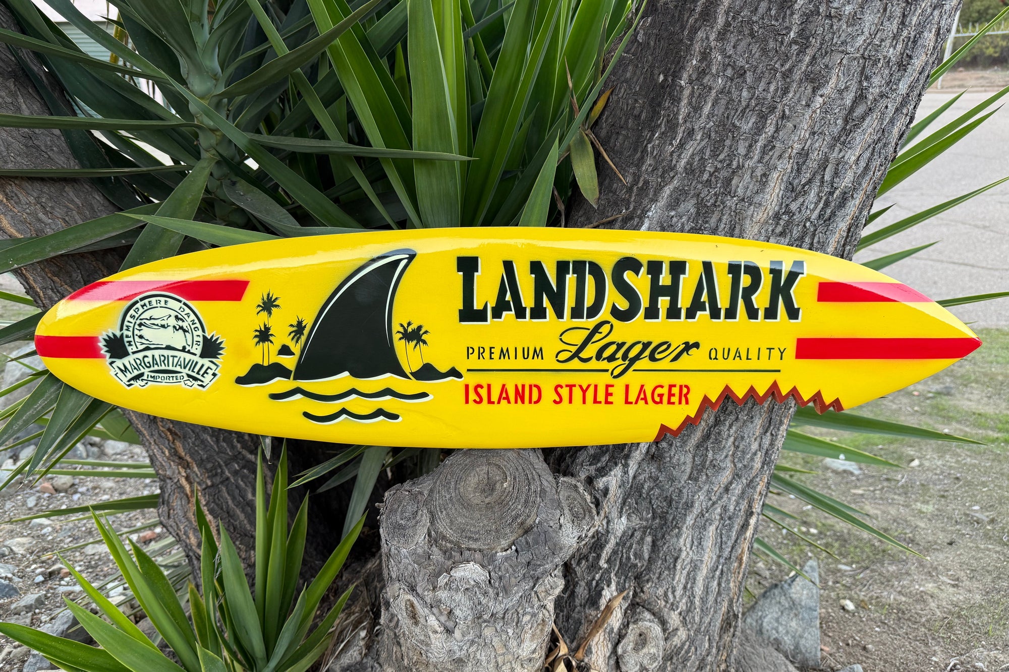 Yellow Landshark Lager surfboard-shaped sign against a tree
