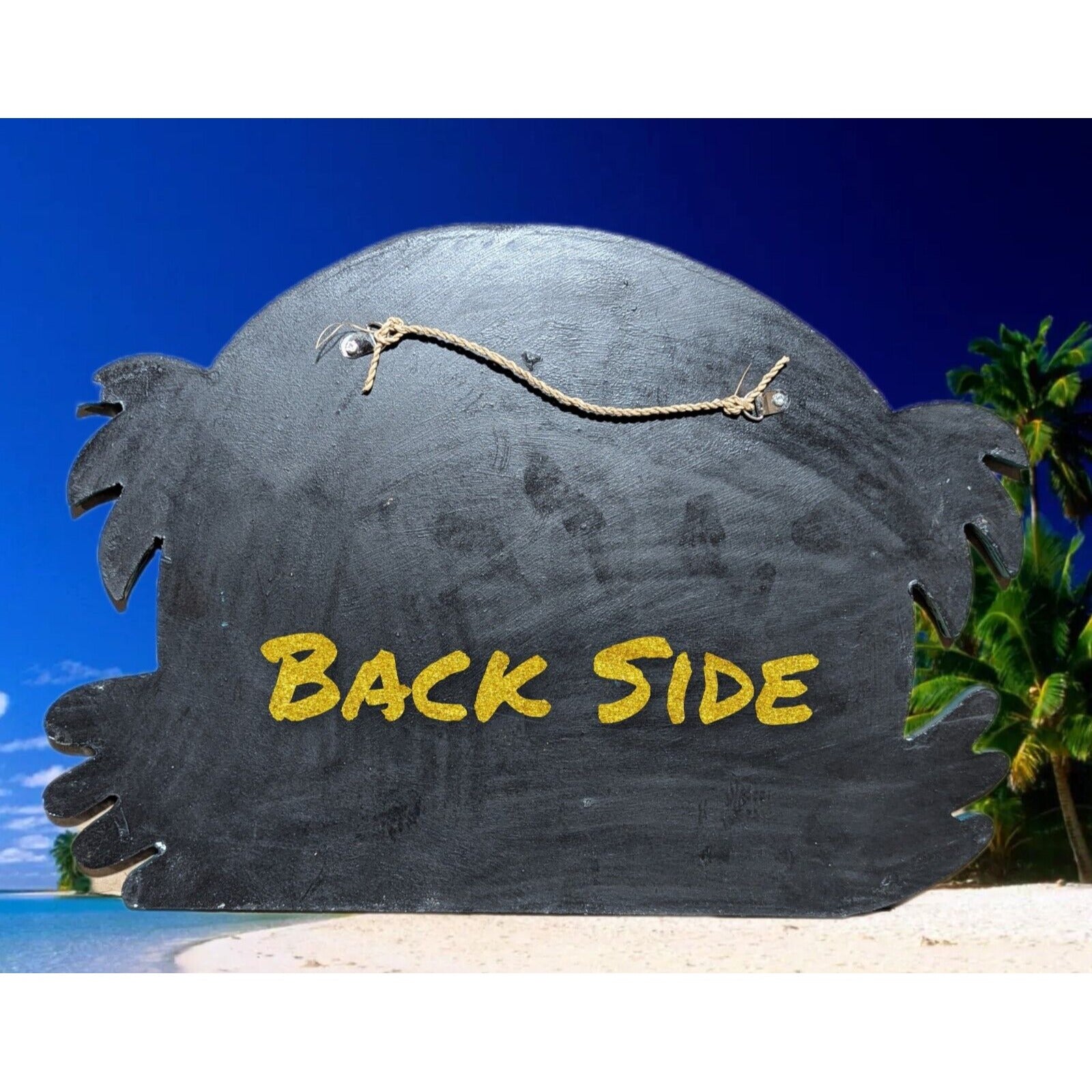 Black wooden sign on a tropical beach reading BACK SIDE in yellow