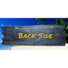 Dark wooden sign with yellow 'BACK SIDE' text on a sunny tropical beach with palm trees.