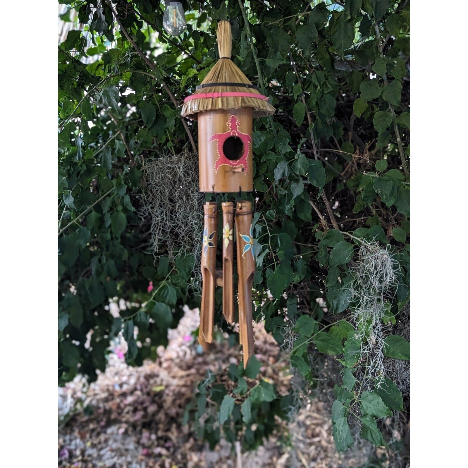 Bamboo wind chime with straw roof hanging from a tree among green leaves