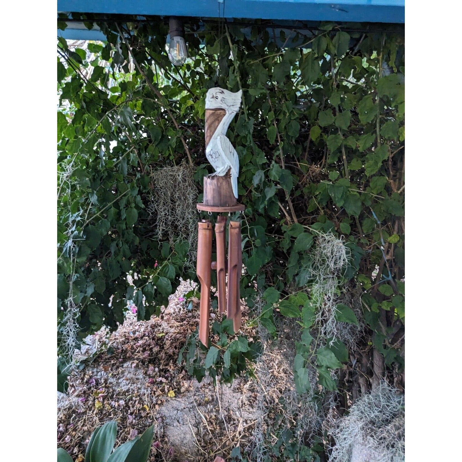 bamboo wind chime with a carved white bird on top, hanging from a wooden post in a garden