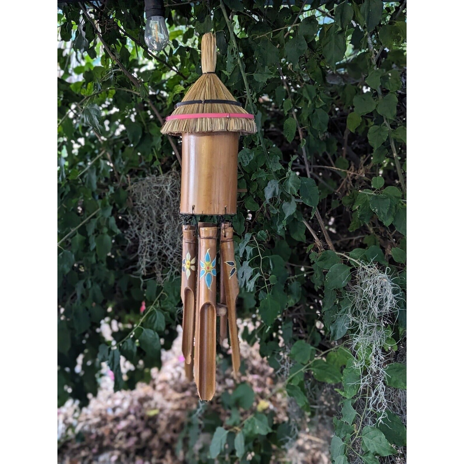 Bamboo wind chime with painted flower designs hanging from a leafy tree