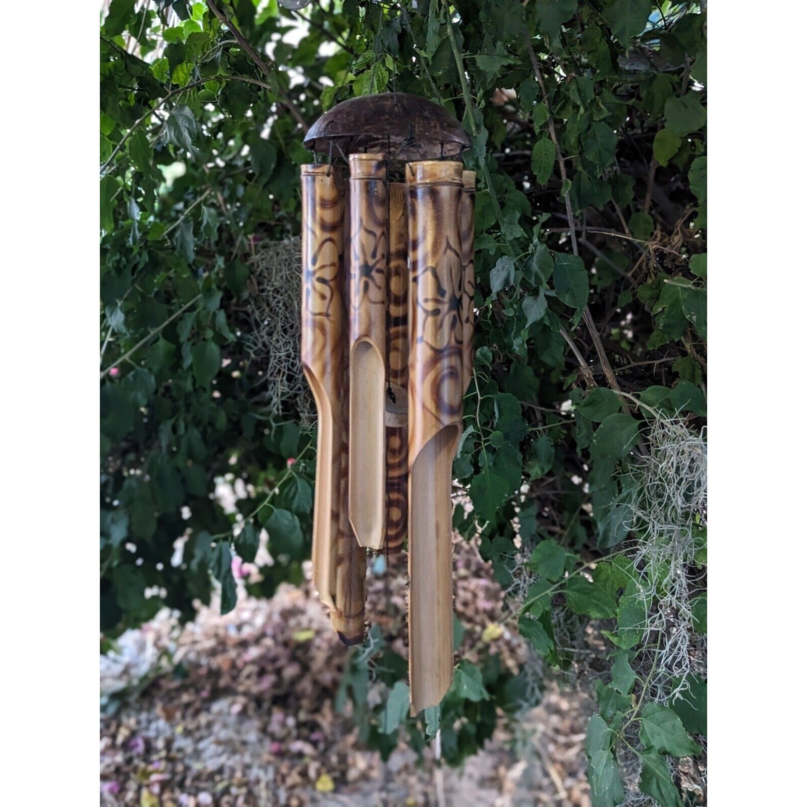 Bamboo wind chime with patterned tubes hanging among green leaves in a garden