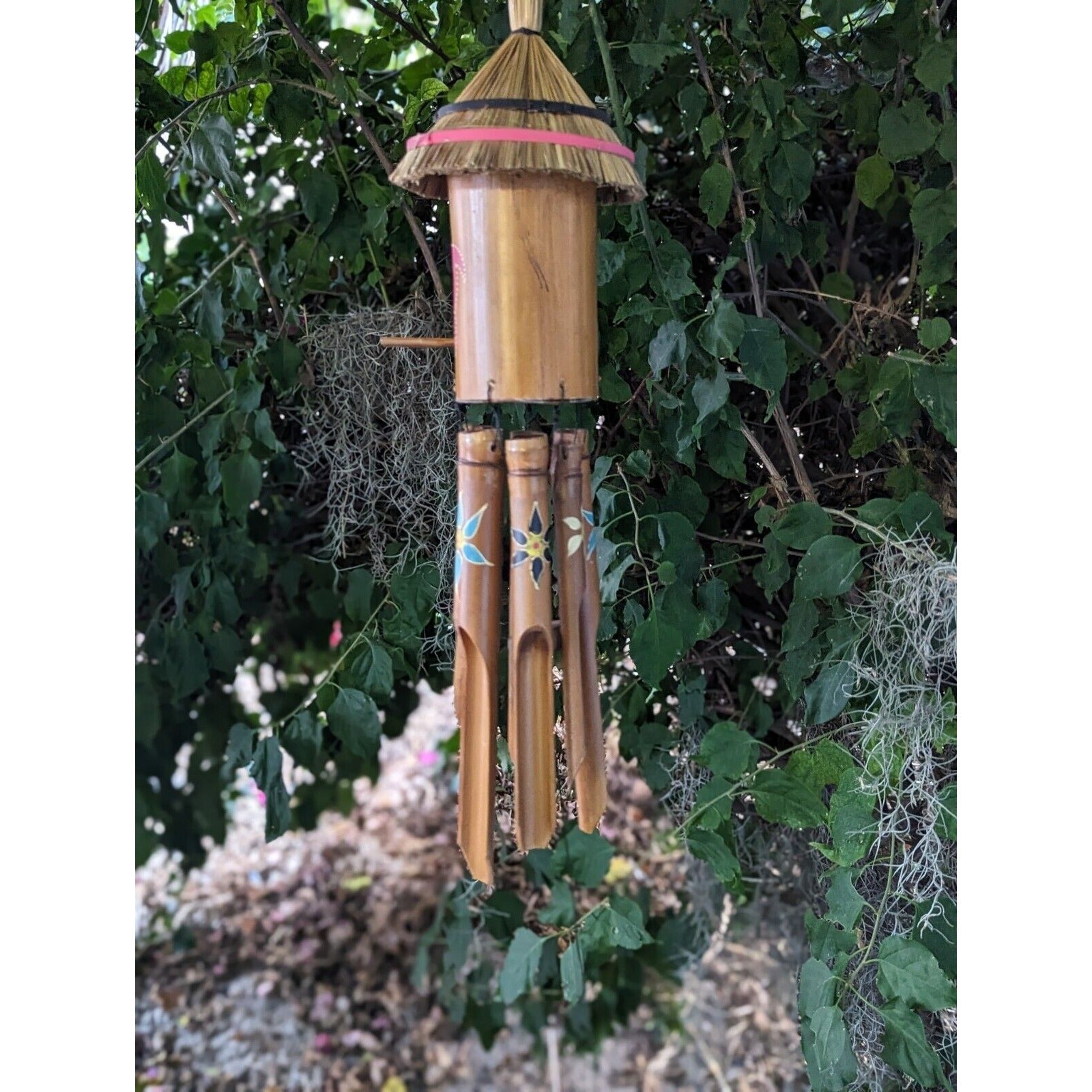 bamboo wind chime with four decorated tubes hanging in a leafy garden
