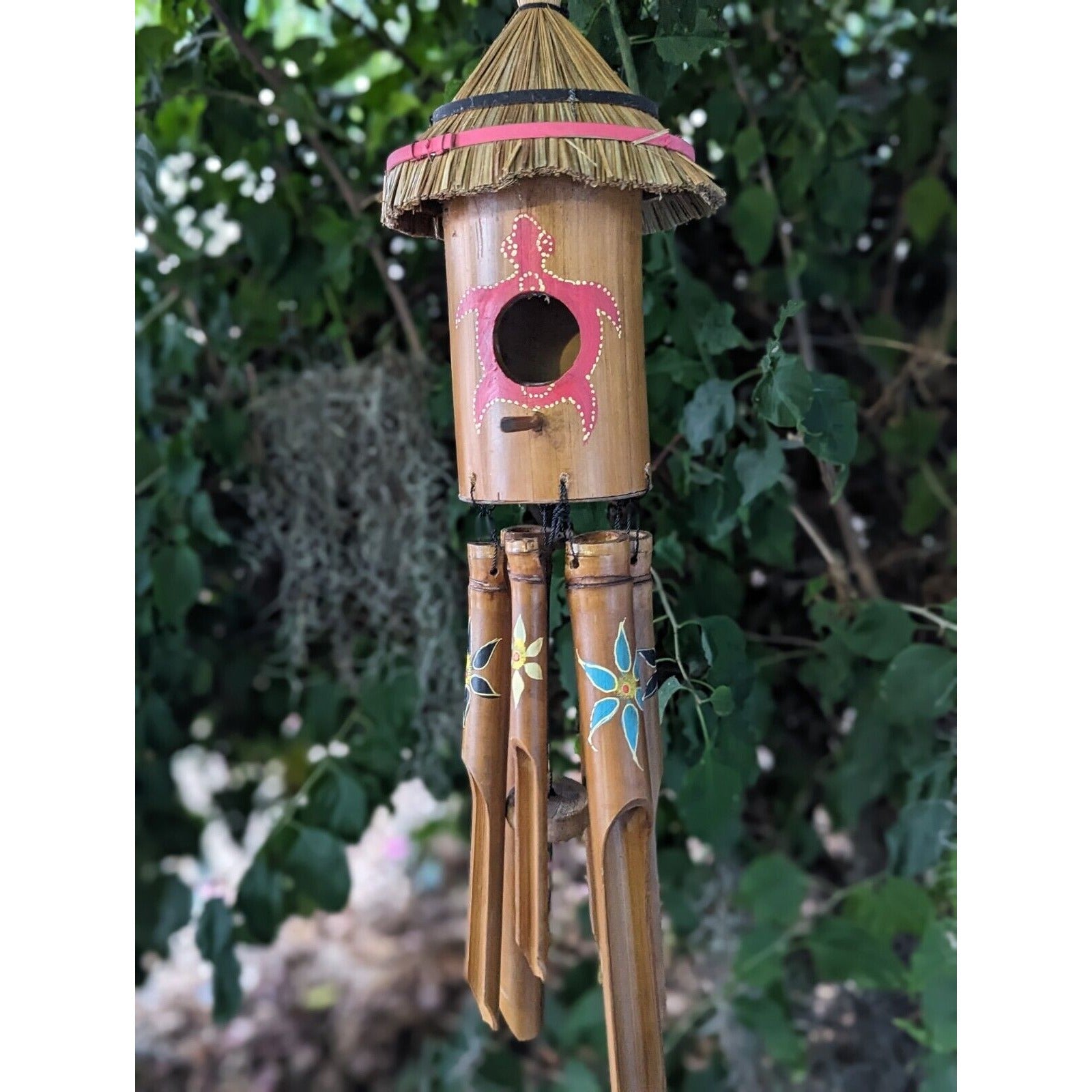 bamboo wind chime with straw roof and pink painted design hanging in a garden