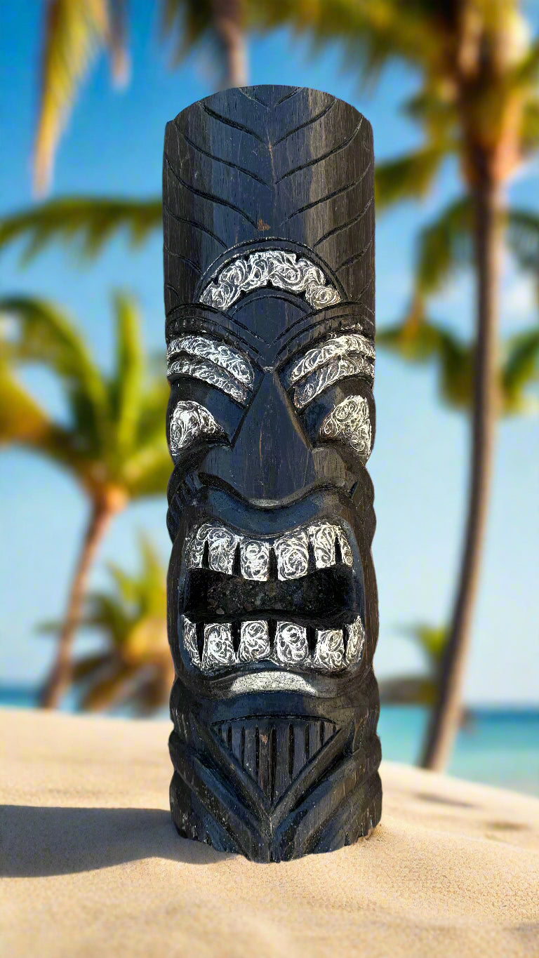 black carved tiki statue on a sandy beach with palm trees in the background.