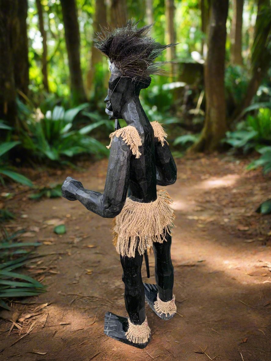 Black carved wooden tribal statue with spiky hair and grass skirt in a forest
