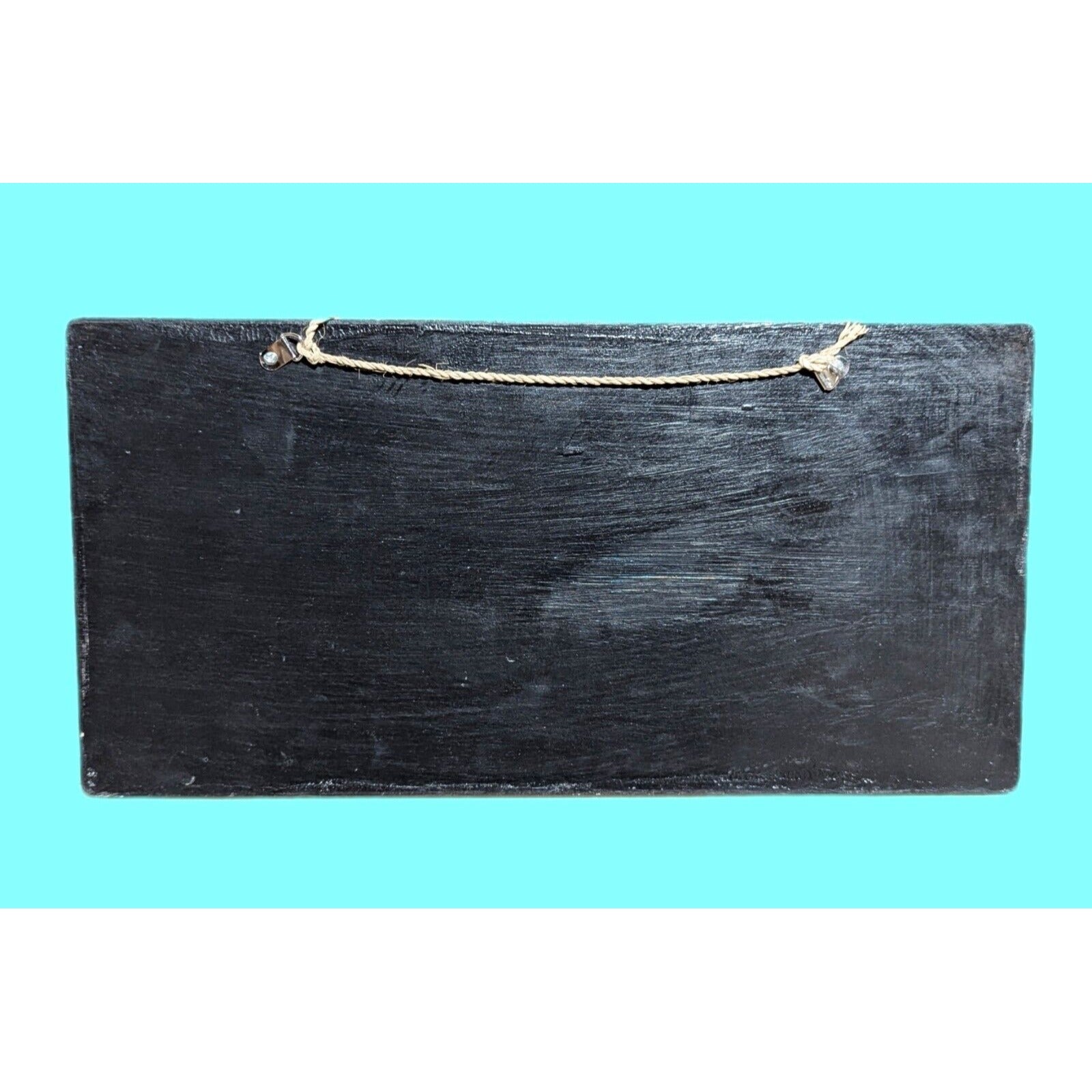 Black hanging chalkboard with rope on turquoise background.