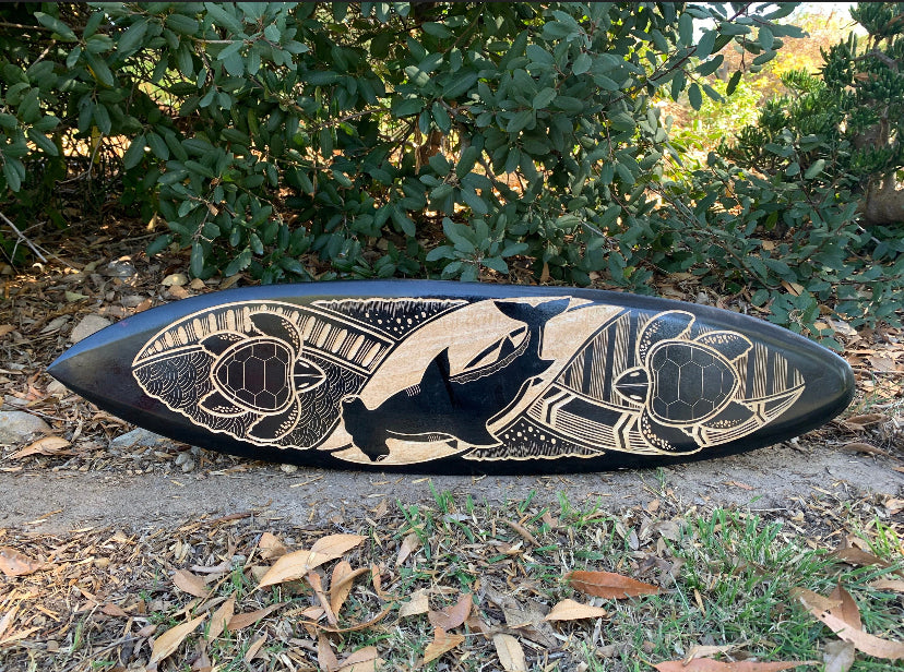 Black longboard with beige carved sea-life design featuring turtles and a whale.