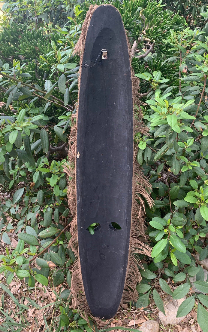 Black longboard with rope-wrapped edges leaning against green bushes