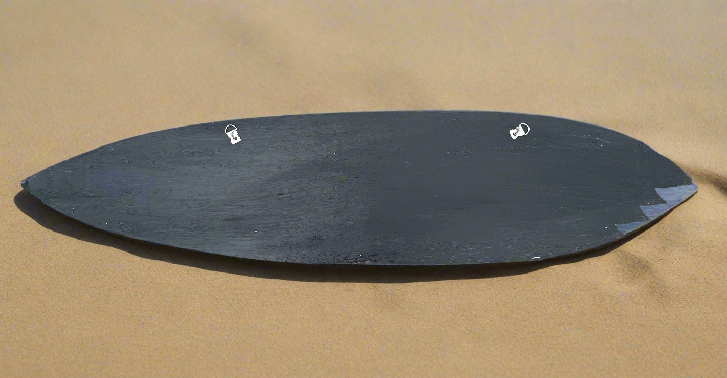 Dark oval-shaped surfboard on sandy beach with two small white clips on top