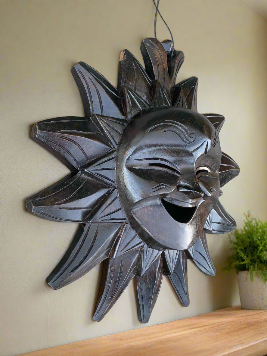 Black wooden sun mask with a joyful smiling face hanging on a wall