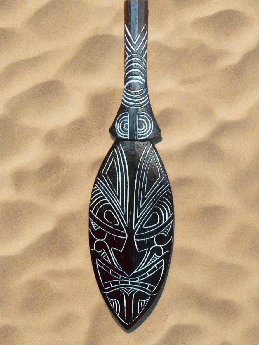 Black wooden carved paddle with white geometric Maori-style designs on a tan background.