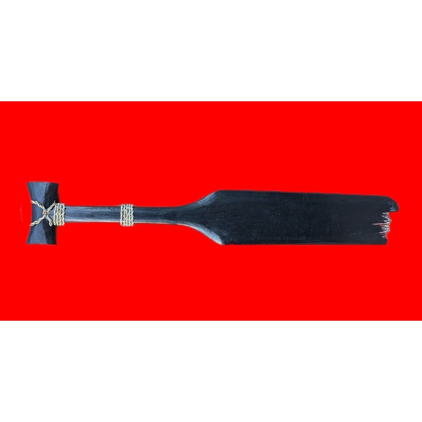 Black wooden paddle with a frayed blade on a red background