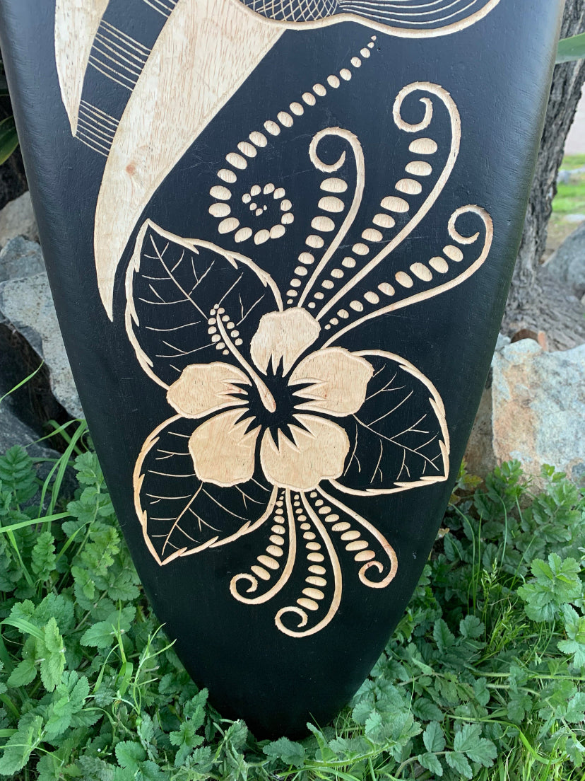 Black wooden panel featuring a beige hibiscus flower carving with decorative swirls
