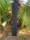 Tall black wooden post standing among green palm fronds.
