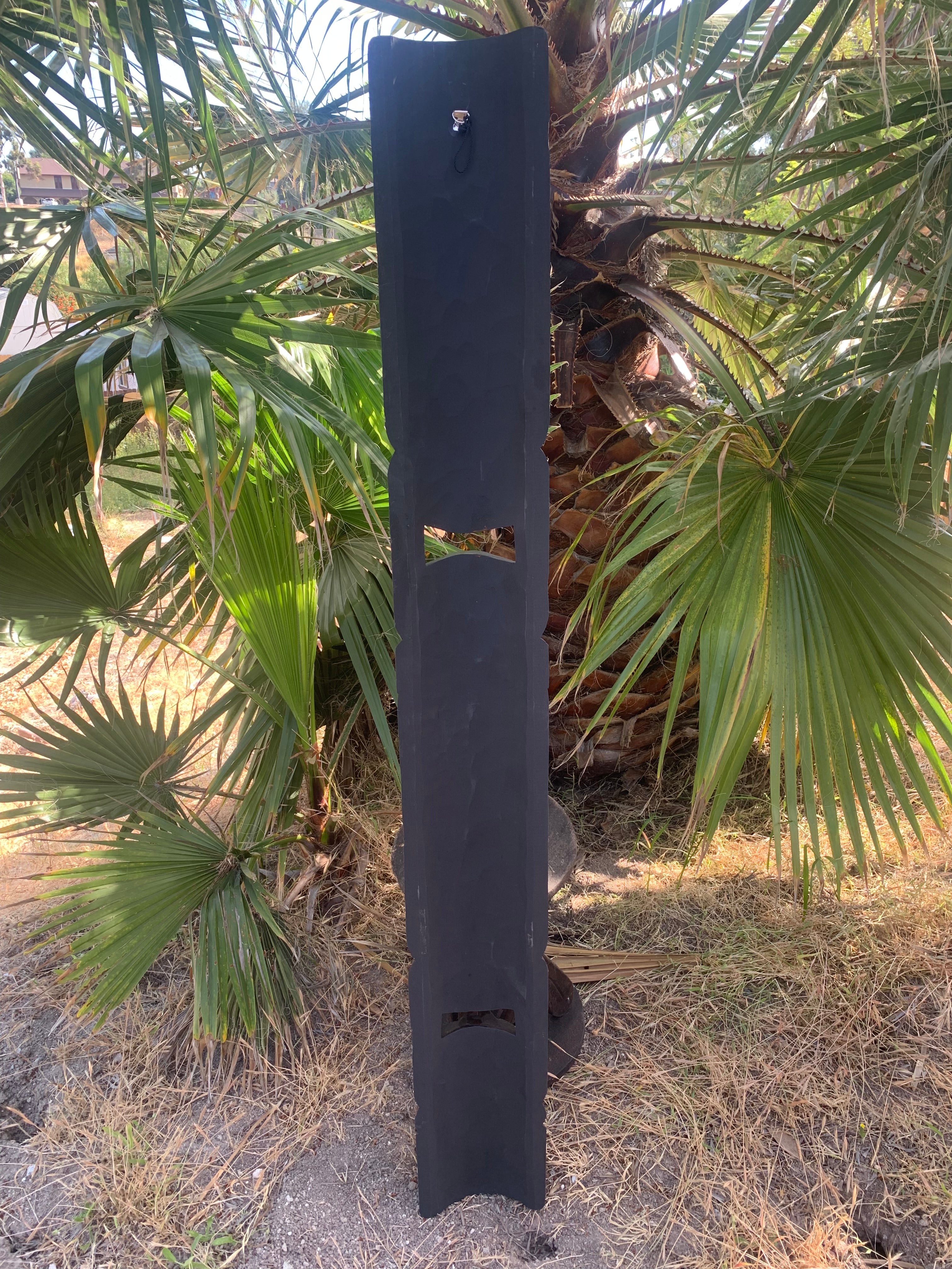 Tall black wooden post with decorative cutouts beside palm trees outdoors