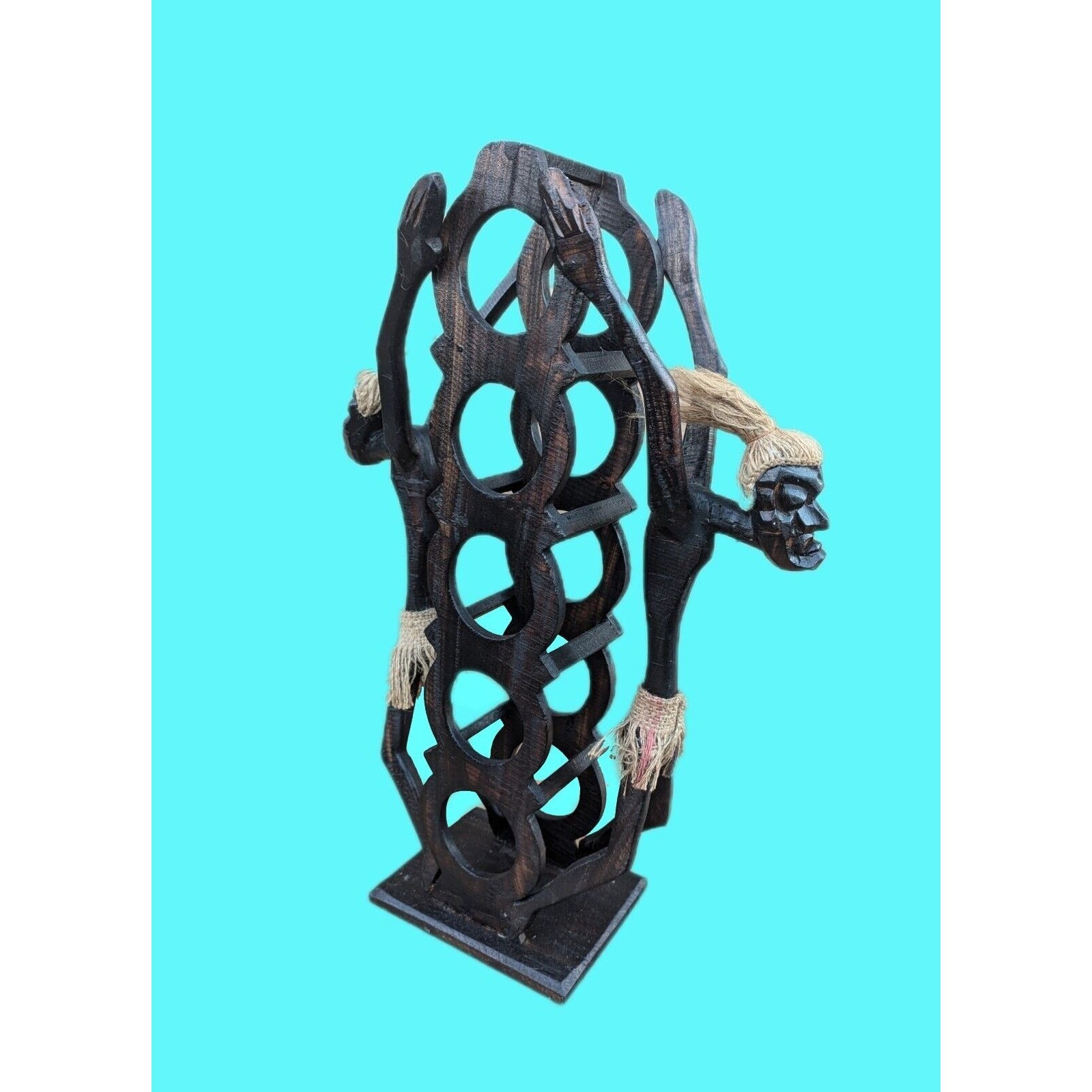 Abstract black wooden sculpture with circular cutouts and rope accents on turquoise background.