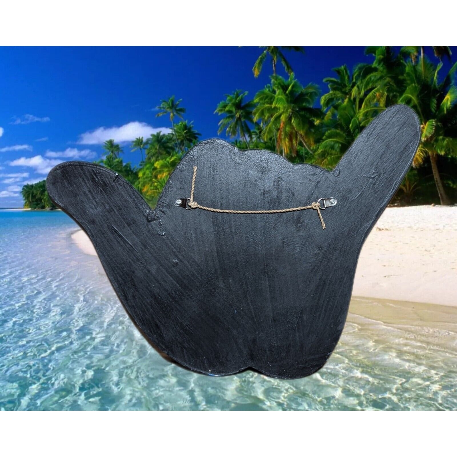 Large black wooden signboard with rope on a tropical beach with palm trees and turquoise water