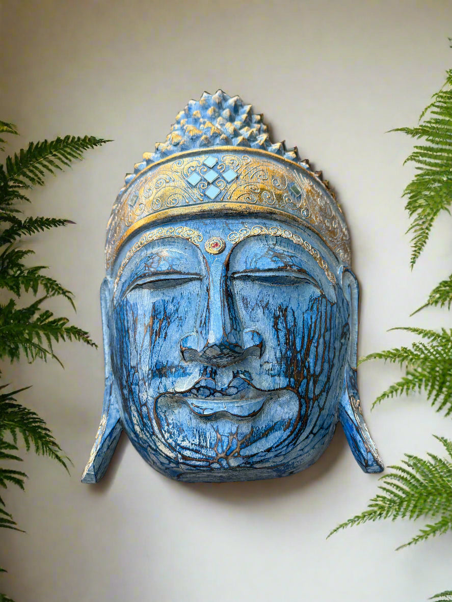 Blue Buddha head statue with gold detailing, surrounded by green ferns.