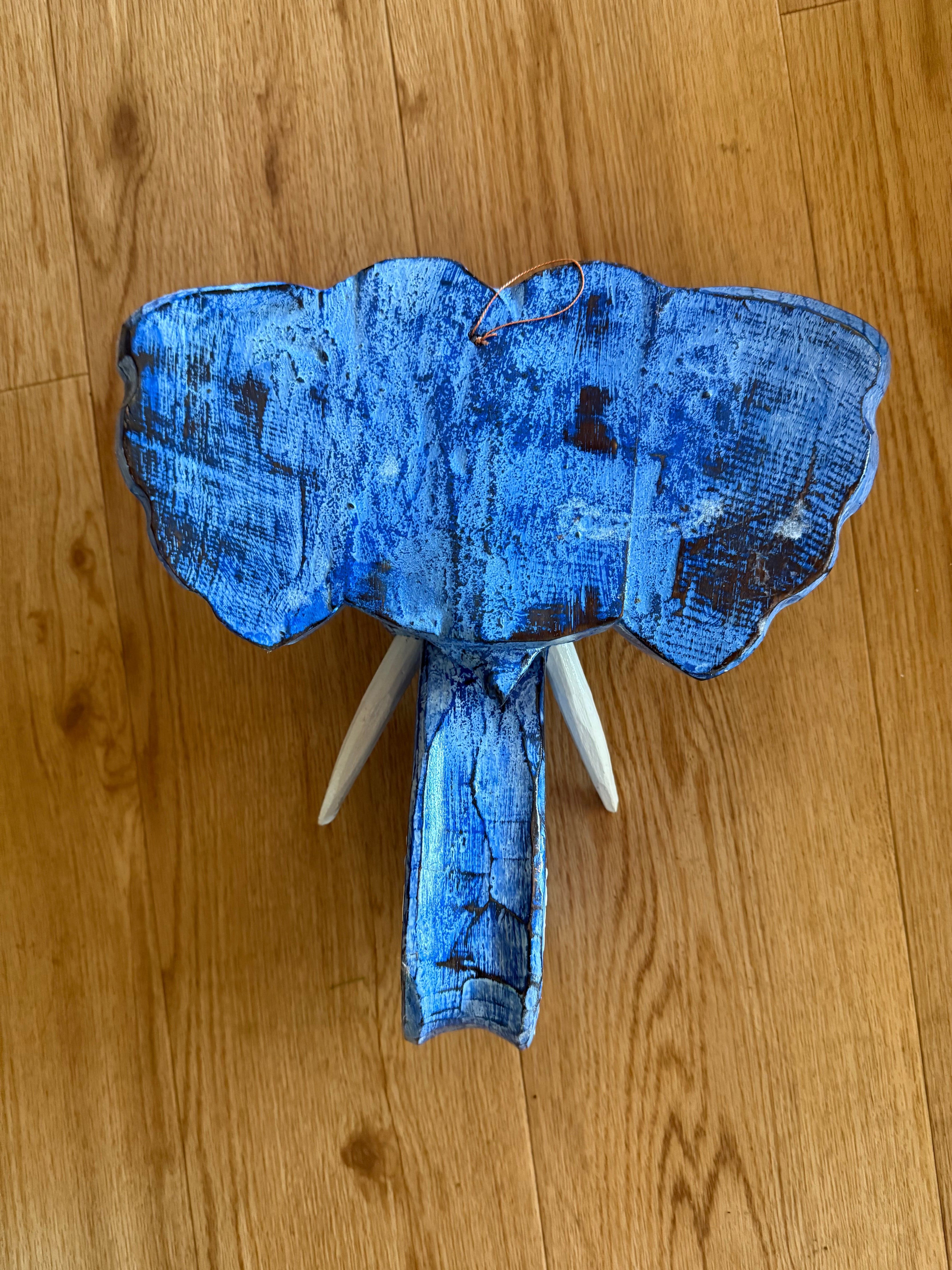 Blue-painted wooden elephant head sculpture with trunk on wooden floor