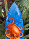 Blue surfboard featuring an orange octopus illustration with circular bubbles.