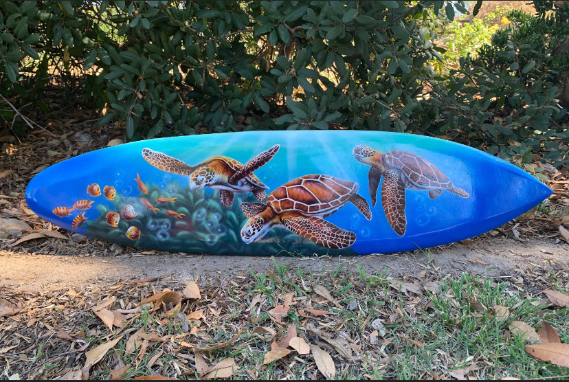 Blue surfboard with sea turtle artwork lying on the ground.