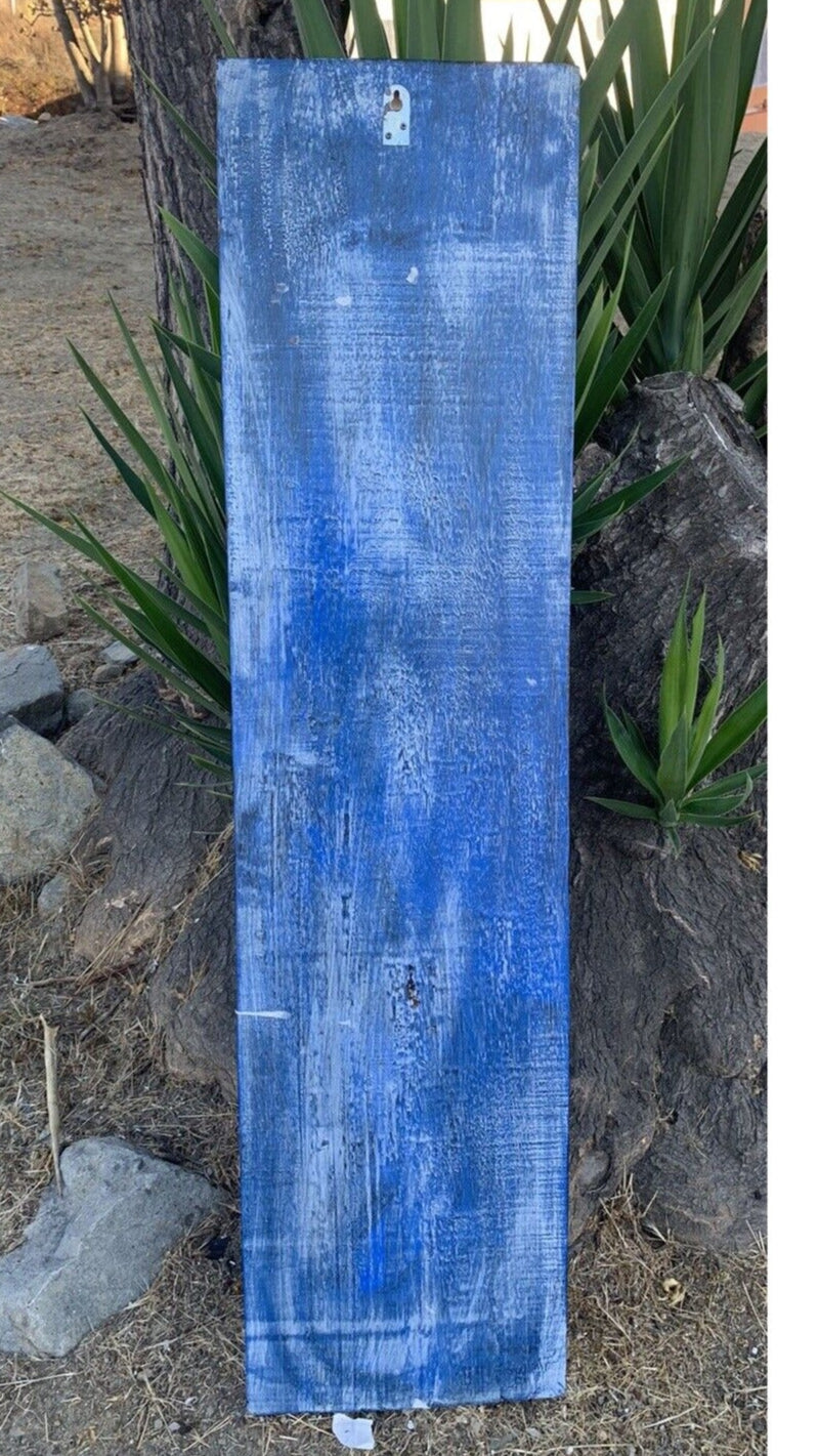 Blue weathered wooden plank outdoors with green plants in the background