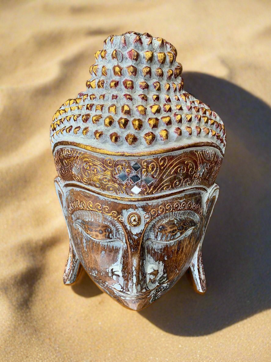 Buddha head statue with ornate gold carvings on sandy surface